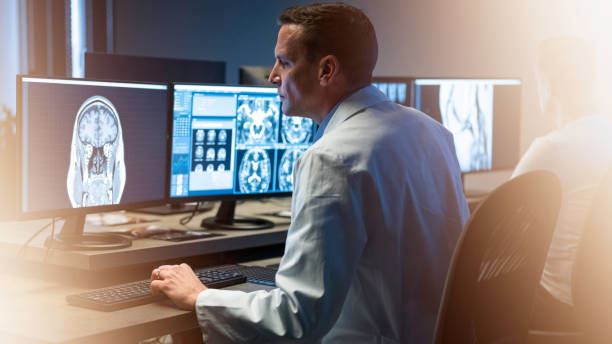 istock Man working on computer with multiple monitors. Analyzing medical scan of brain. 1320844651
