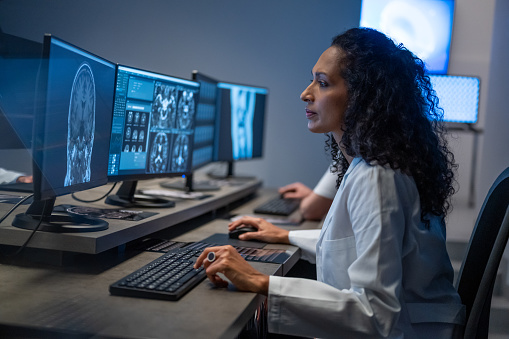 Side view of Hispanic woman working on computer. Female doctor analyzing medical scan result. Examination at specialized medical clinic, diagnosis and healthcare concept.