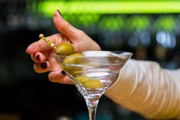 istock Female hand inserted olives impaled on toothpick into Martini drink. 1320844694