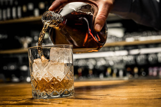 versando un bicchiere di whisky. bottiglia di tenuta della mano maschile con alcol di lusso. - whisky alcohol pouring glass foto e immagini stock