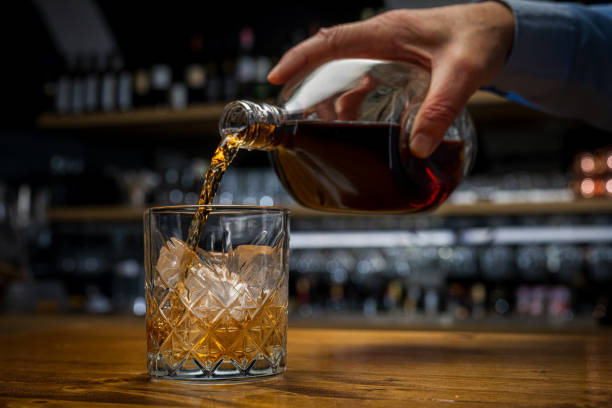 man preparing drink, pouring old scotch whiskey into glass standing on wooden table. - action alcohol alcoholism bar imagens e fotografias de stock