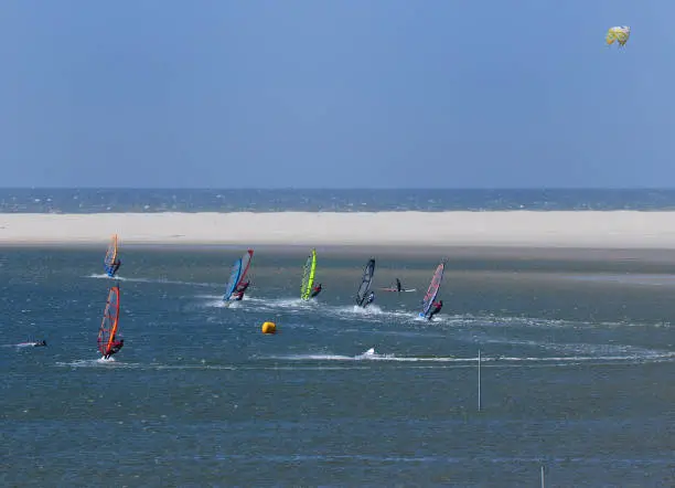 Young People Windsurfing In A Small Bay On The East Frisian Island Borkum On A Sunny Spring Day With A Clear Blue Sky