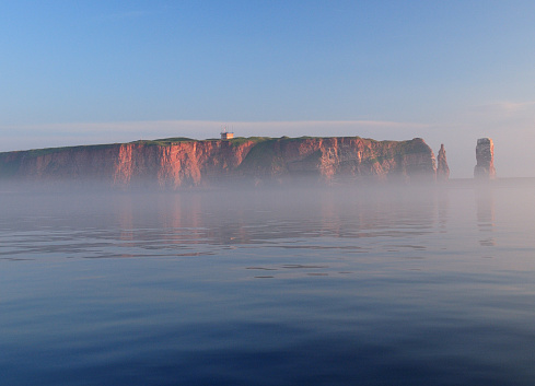 View From The Foggy Sea To The Rusty Cliffs And The Famous Sea Stack Lange Anna Of The North Sea Island Helgoland On A Sunny Summer Day With A Clear Blue Sky