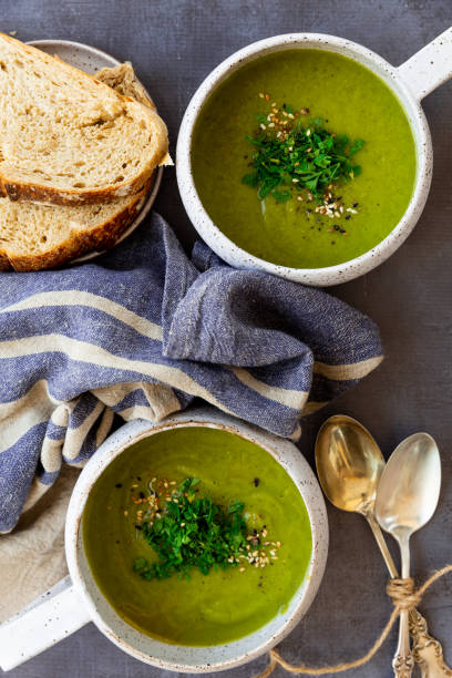 istock Green soup with toppings in white ceramic, napkins, spoon, bread slices on a gray surface 1320860347
