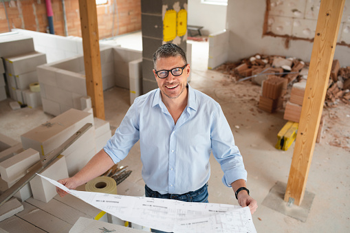 man with black glasses and blue shirt is looking at plan and is checking construction progress on building site in loft, attic in a house
