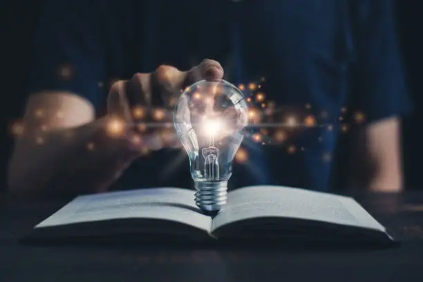 Photo of Glowing light bulb and book or text book with futuristic icon. Self learning or education knowledge and business studying concept. Idea of learning online class or e-learning at home.