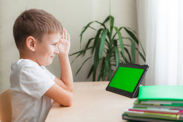 istock smart school boy siting at desk and looks at tablet. A child pulling hand to answer. 1320886077