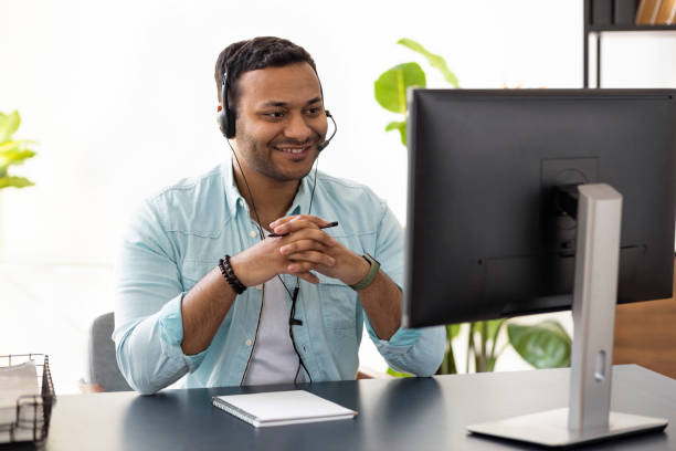 istock Online communication. Happy young Indian millennial man uses computer for video call or video meeting, call center employee, advises clients online, support operator 1320889482