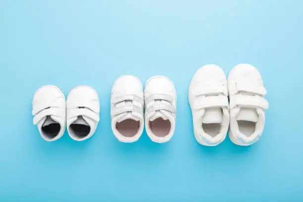 New white sport shoes on light blue table background. Pastel color. Closeup. Different sizes. Concept of child growing. Top down view.