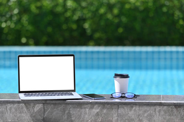 istock Computer laptop with blank screen, coffee cup and glasses near the swimming pool. 1320899401