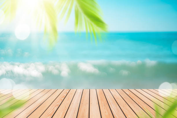 istock Blur tropical beach with bokeh sun light wave and palm tree on copy space empty old wood table abstract background. 1320900309