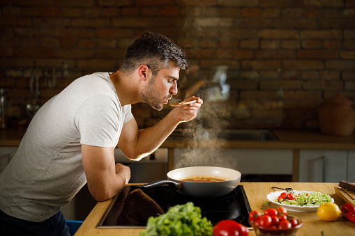Profile view of a man tasting his food while cooking lunch in the kitchen.