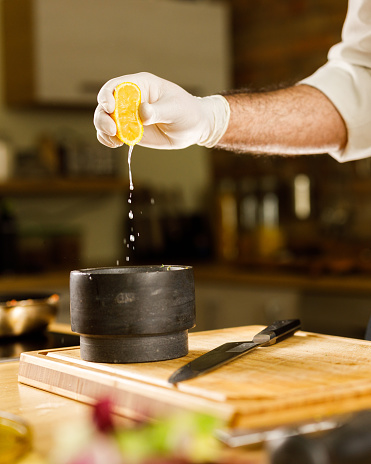 Unrecognizable professional chef squeezing lemon juice while adding it to his recipe into a mortar and pestle.