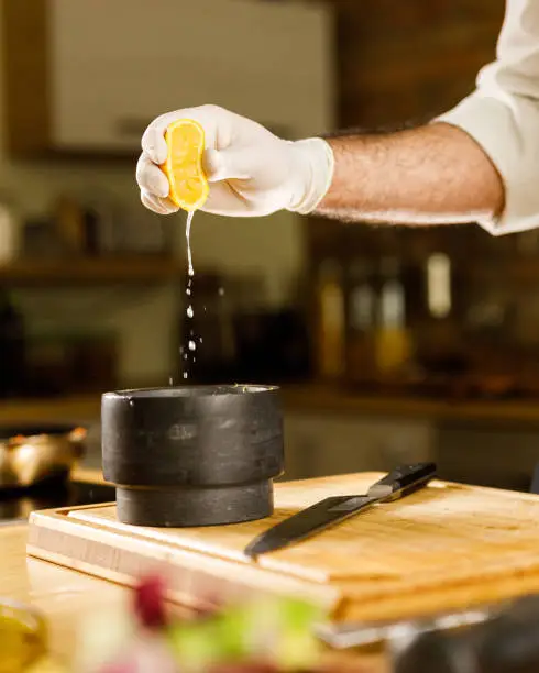 Photo of Unrecognizable chef squeezing lemon juice into mortar and pestle.