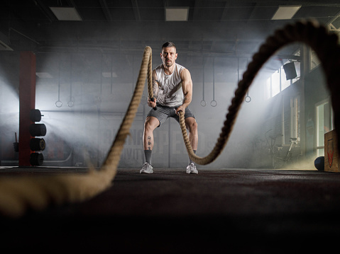 Muscular build athletic man having cross training with battle ropes in a health club. Copy space.