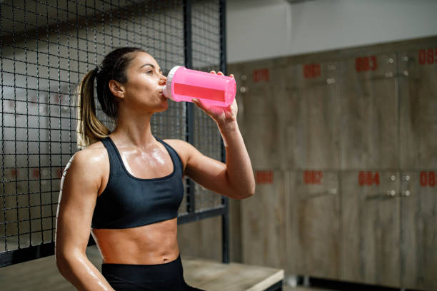 Thirsty female athlete drinking water on a break at gym's locker room.
