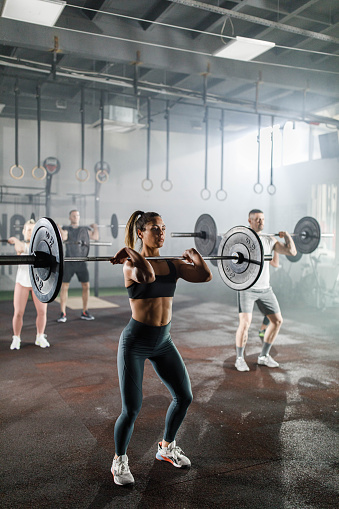 Group of athletes having weight training with barbells in a gym. Focus is on woman in the foreground.