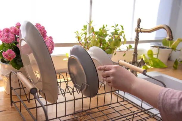 Photo of Woman puts beautiful plates on drainer after washing on the kitchen in the morning