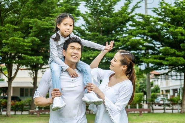 Portrait of asian happy family of three having fun together in park, little daughter sitting on father back and mother smile walking and having fun moments good time in summer park at home retrato de la familia asiática feliz de tres divirtiéndose juntos en el parque, la hija pequeña sentada en la espalda del padre y la sonrisa de la madre caminando y teniendo momentos divertidos buen momento en el parque de verano en casa