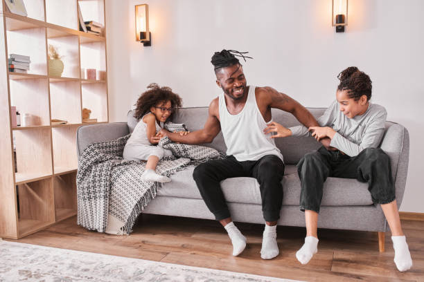 istock Funny father playing with his schoolgirl daughters while sitting together on sofa 1320910555