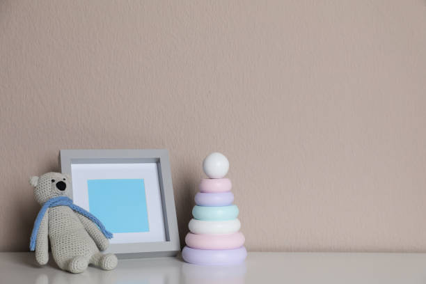 istock Empty photo frame, toy bear and ring pyramid on white table near grey wall. Space for design 1320910659