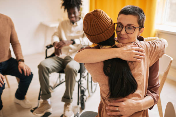 Women Embracing at Therapy Session Portrait of female psychologist embracing young woman during therapy session in support group, copy space group therapy stock pictures, royalty-free photos & images