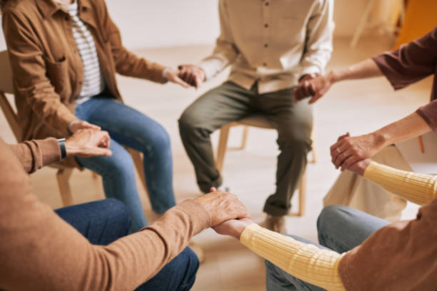 Holding Hands in Support Circle Warm toned closeup of people holding hands in circle during therapy session in support group, copy space group therapy photos stock pictures, royalty-free photos & images
