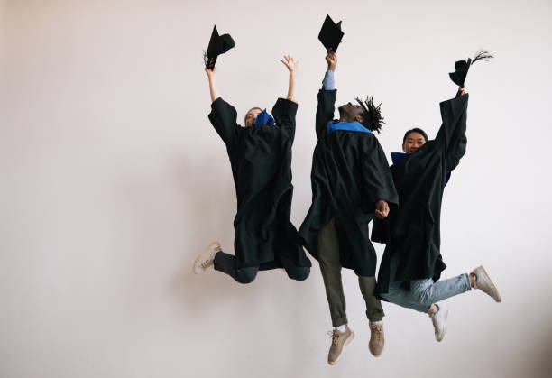 excited college graduates jumping - graduation adult student mortar board student imagens e fotografias de stock