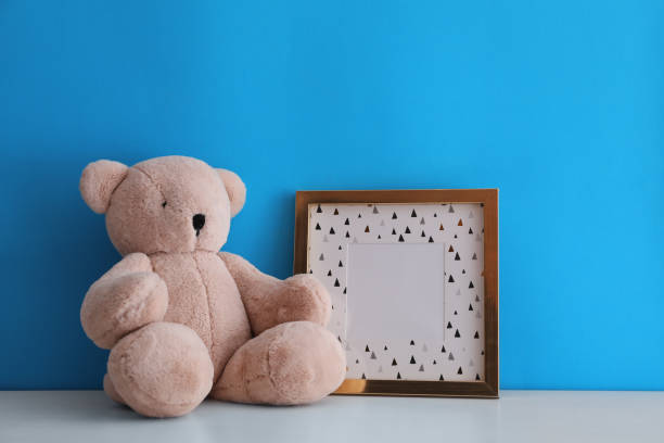 istock Empty photo frame and teddy bear on white table near light blue wall. Space for design 1320910842