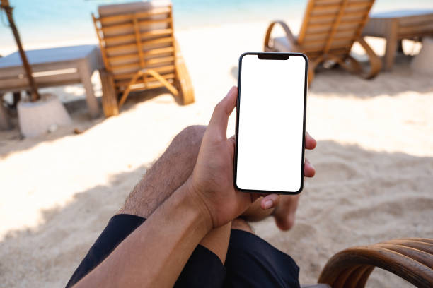 istock a man holding mobile phone with blank desktop screen while sitting on the beach 1320918532