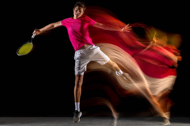 One man, male tennis player training isolated in mixed neon light on dark background. Concept of sport, team competition. Shot in jump. Young professional tennis player, sportsman in sportswear playing tennis in mixed neon light on dark background. Concept of motion, power, speed, healthy lifestyle, professional sport. temporal aliasing stock pictures, royalty-free photos & images