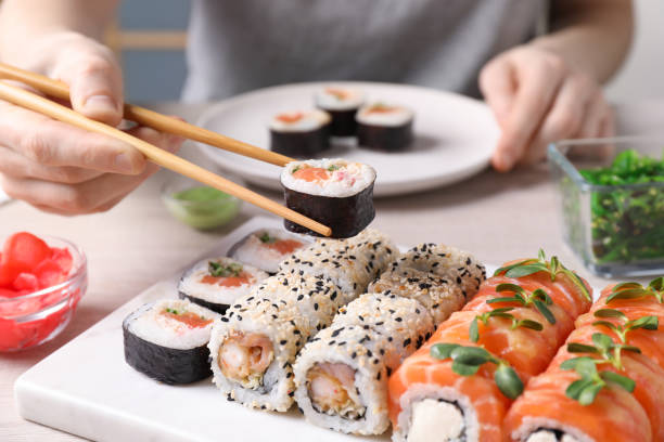 donna che prende gustoso rotolo di sushi con salmone da set a tavola, primo piano - sushi foto e immagini stock