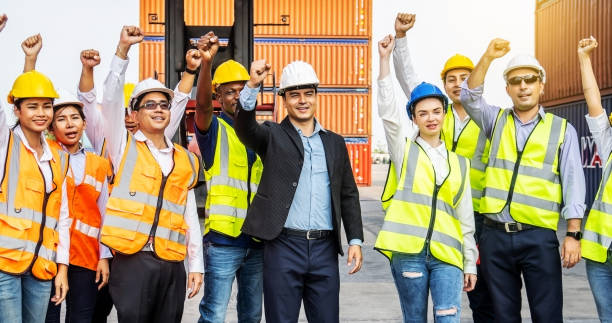istock Cargo container workers or group of employee express raised their hands to express their joy to celebrate the success of their work. With a crane and a shipping container pile in the background 1320922723