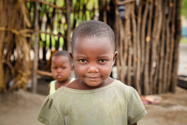 pequeños hermanos africanos de pie en su patio - africa child village smiling fotografías e imágenes de stock