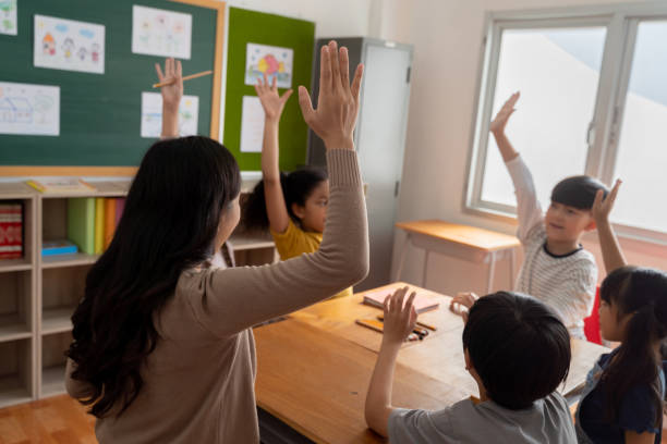 istock Asian school teacher with students raising hands 1320924371