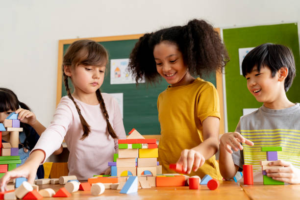 Children playing with wooden blocks in classroom Group of multiethnic school friends using toy blocks in classroom, education, learning, teamwork. Children playing with wooden blocks in classroom primary school stock pictures, royalty-free photos & images