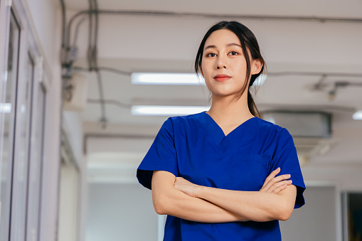 Portrait of young and beautiful confident nurse wearing uniform standing with arms crossed in hospital looking at camera with pride in serving patients infected with covid-19