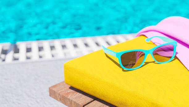 sunglasses on deck chair close-up of sunglasses on deck chair with towel and pool out of focus in the background. 3d render chaise longue stock pictures, royalty-free photos & images
