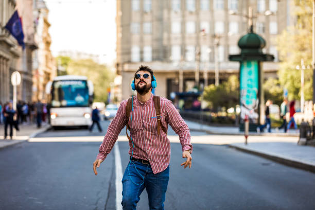istock Happy man in earphones using mobile phone while dancing on street 1320928989