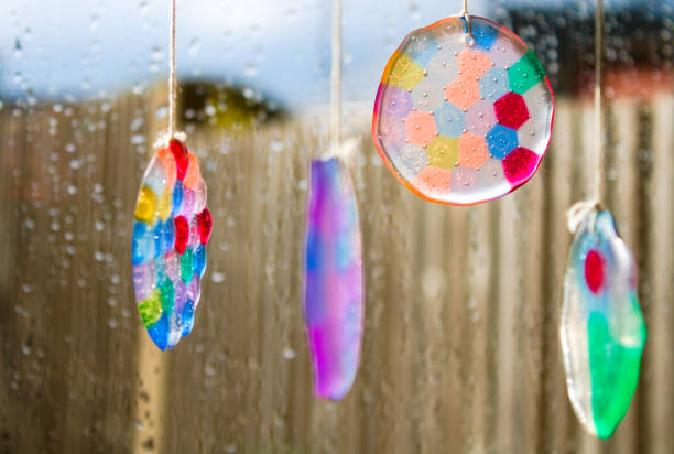 colorido timbre de viento en la ventana con gotas de lluvia y jardín fuera de foco en el fondo - carillon fotografías e imágenes de stock