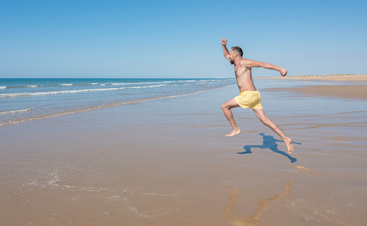 Young hipster man with a beard in a yellow swimsuit runs and jumps into the sea on a lonely beach. leisure and vacation concept