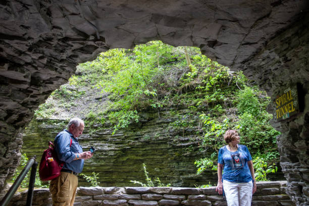 Couple by Spiral Tunnel at Watkins Glen State Park Watkins Glen, USA - May 22, 2021. A senior man looking at his cell phone and a senior lady looking at something on right outside the Spiral Tunnel at Watkins Glen State Park, Finger Lakes Region, New York, USA watkins glen stock pictures, royalty-free photos & images