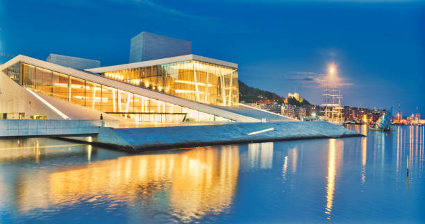 Panoramic view of the modern Opera House of Oslo, Norway und a full moon. In 1999, after a long national debate, the Norwegian legislature decided to construct a new opera house in the city. In 2008 it was opened y His Majesty King Harald, Queen Margrethe II of Denmark. Until today more than a million visitors every year since then visit this famous landmark of norway. The angled exterior surfaces of the building are covered with marble from Carrara, Italy and white granite and make it appear to rise from the water. It is the largest cultural building constructed in Norway.