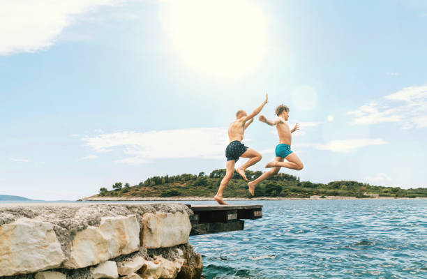 istock Son with Father having a fun on a merry vacation days on Adriatic sea coast. They dressed swimming trunks jumping to the waives from the boat pier. Family time, fatherhood or childhood concept image. 1320941197