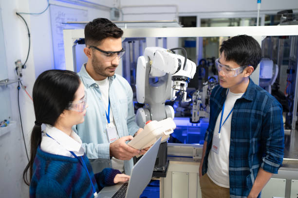 istock Caucasian male engineer holding a robot controller demonstrating the work of robotic machine to Asian male engineer and Asian female apprentice engineer 1320941514