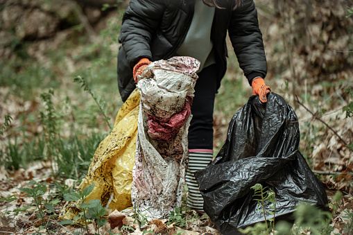 A volunteer girl with a garbage bag cleans up garbage in the forest.