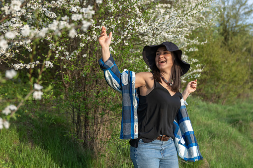 Attractive cheerful girl in a hat among the flowering trees in the spring, in a casual style.