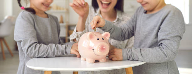 Happy mother and children saving up money for their future plans and dream projects Happy mother and little children saving up money for future plans and dream projects. Family finance, budget management, financial literacy for kids concepts. Website design header, piggy bank closeup literacy photos stock pictures, royalty-free photos & images
