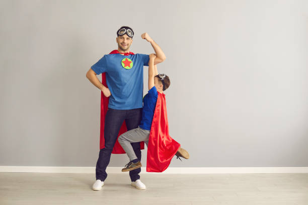 happy young father and little son dressed in superhero capes having fun together - superhero humor men cape imagens e fotografias de stock