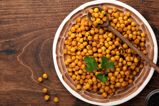 istock Fried chickpeas with turmeric in ceramic plate on an old wooden table background. Roasted spicy chickpeas or Indian chana or chole, popular snack recipe. Top view. 1320946082
